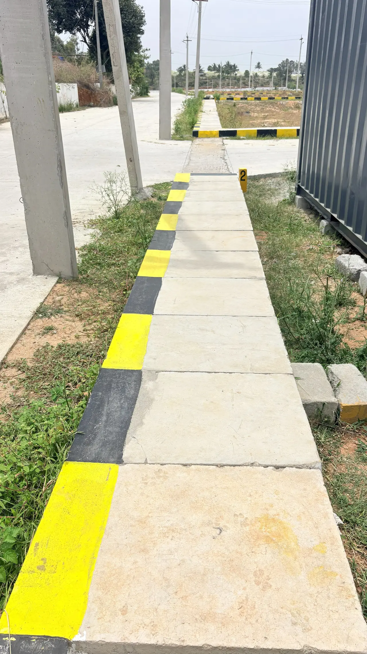 Concrete footpath with painted kerb running past street-light poles towards the layout beyond.