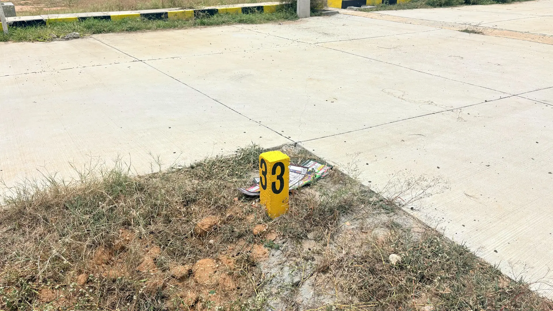 Yellow numbered boundary stone marking plot 33 at the corner of two concrete roads.