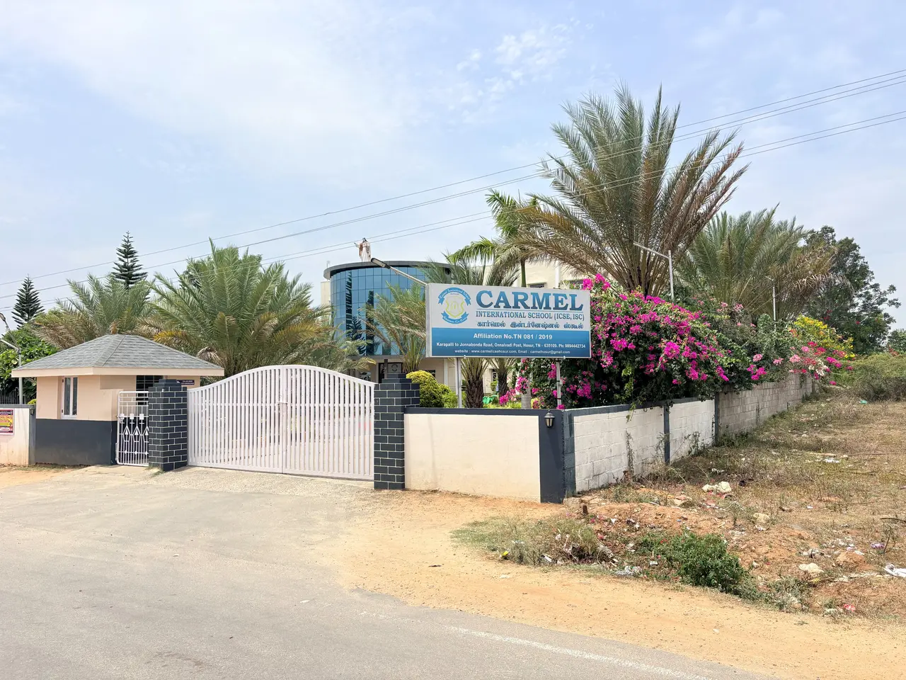 The gated entrance of Carmel International School on the Karapalli road, with its signboard, palms and flowering bougainvillea along the wall.