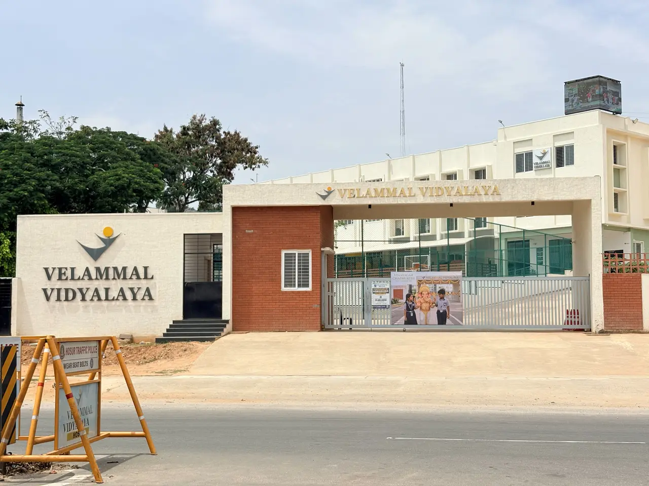 The entrance arch and signboard of Velammal Vidyalaya beside the road, with the school buildings behind the gate.
